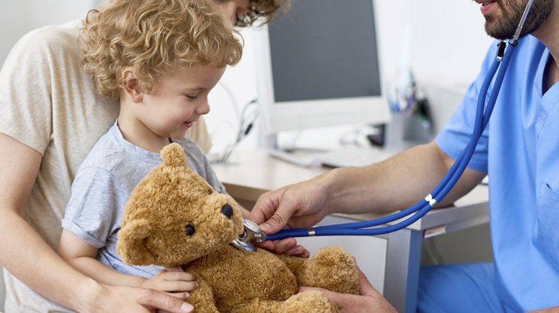 Un bambino con l'orsacchiotto visitato dal medico